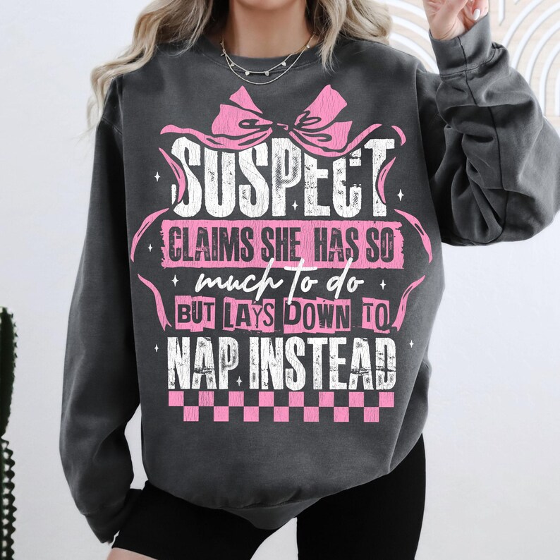 Pu&ograve; includere: Felpa grigia con un fiocco rosa e testo bianco che recita "SUSPECT CLAIMS SHE HAS SO much TO DO BUT LAYS DOWN TO NAP INSTEAD".