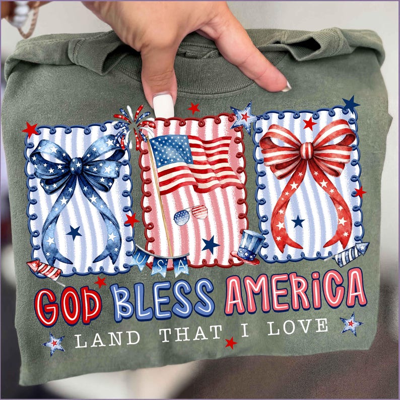 Puede incluir: Camiseta verde oliva con gr&aacute;ficos patri&oacute;ticos. El dise&ntilde;o incluye tres marcos rectangulares con un lazo azul, una bandera estadounidense y un lazo rojo. El texto "GOD BLESS AMERICA LAND THAT I LOVE" est&aacute; impreso en rojo y azul.