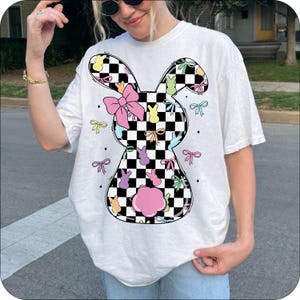 Puede incluir: Camiseta blanca con un dise&ntilde;o de conejo a cuadros. El conejo est&aacute; lleno de caramelos de goma pastel y lazos.