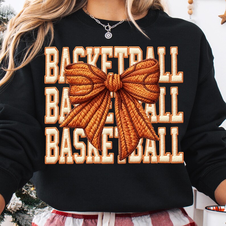 May include: Black sweatshirt with the word "BASKETBALL" in a stacked design, with a large orange bow graphic. The text is in a serif font with an orange outline and a white fill.