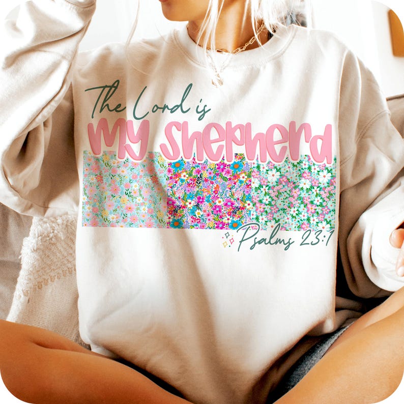 May include: A white sweatshirt with the text "The Lord is My Shepherd" in pink lettering and a floral pattern below. The text "Psalm 23:1" is also included.