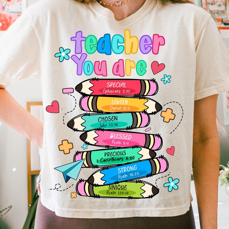 May include: Cream-colored t-shirt with a colorful graphic design. The design features the words "teacher You are" above stacked pencils, each with a different color and a positive adjective like "Special" and "Unique".