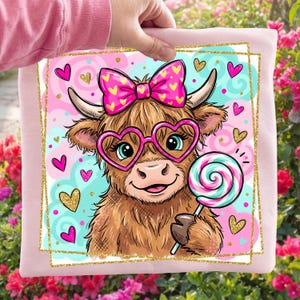 Può includere: Un cuscino rosa con un cartone animato di mucca delle Highlands con occhiali a forma di cuore e un fiocco rosa. La mucca tiene in mano un lecca-lecca. Lo sfondo presenta accenti a forma di cuore rosa, blu e oro.