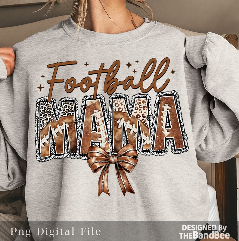May include: Grey sweatshirt with the text "Football Mama" in brown and white lettering. The letters are decorated with brown footballs and leopard print. A brown bow is below the text.