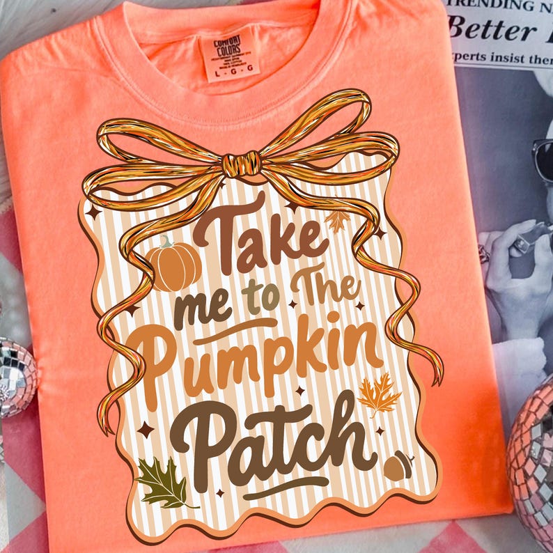 May include: Coral-colored t-shirt with a fall-themed graphic. The design features the text "Take me to The Pumpkin Patch" in brown and orange, along with a pumpkin, leaves, and an acorn. A large bow frames the text.
