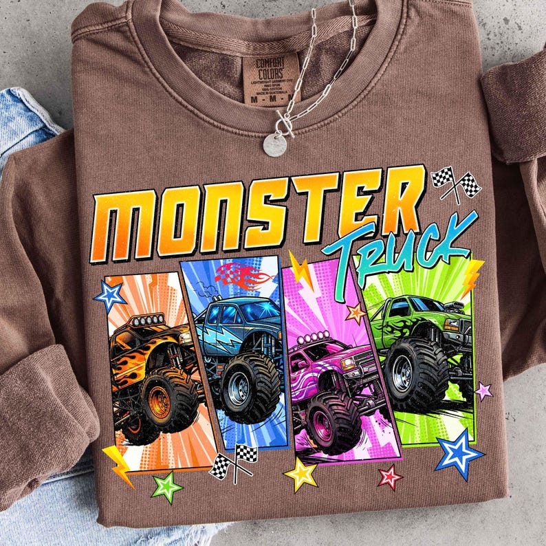 May include: Brown crewneck sweatshirt with a colorful graphic of four monster trucks. The design includes the words "Monster Truck" in a bold, outlined font, along with stars and checkered flags.