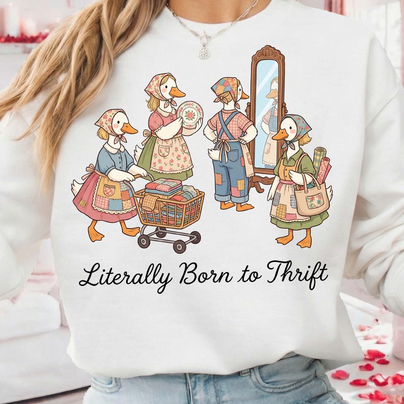 May include: White sweatshirt featuring a whimsical illustration of anthropomorphic geese dressed in vintage clothing, shopping and thrifting. The phrase "Literally Born to Thrift" is printed in black script across the bottom of the design.