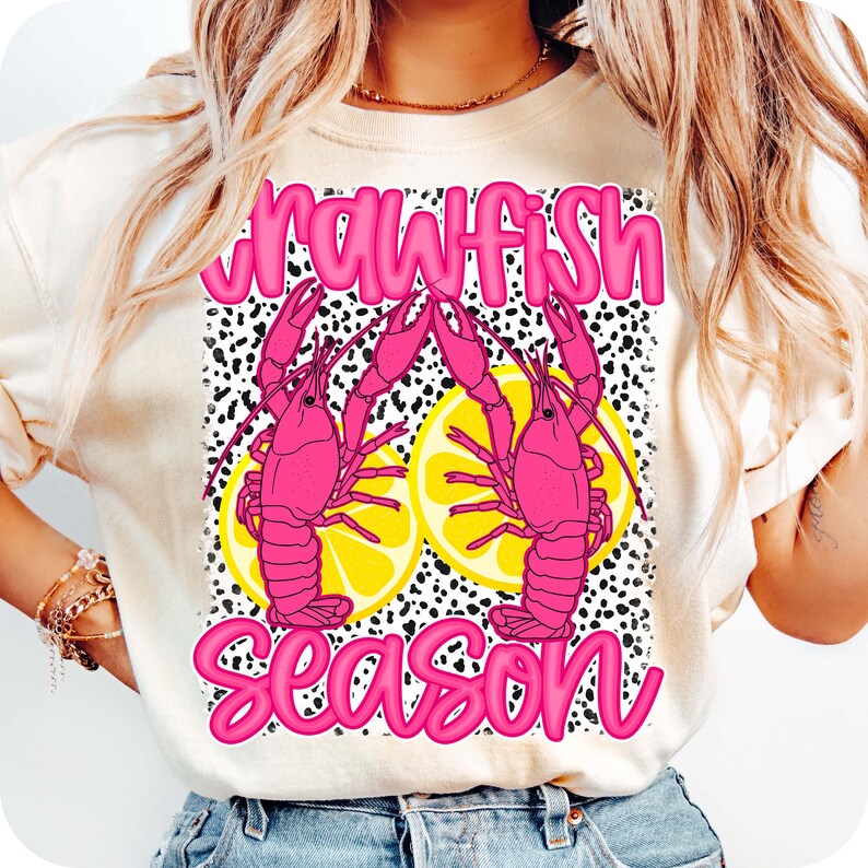May include: A white t-shirt with a pink and yellow graphic design featuring crawfish and lemons. The text "Crawfish Season" is written in pink letters.