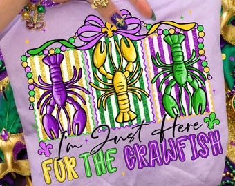May include: A light purple t-shirt featuring three cartoon crawfish in purple, yellow, and green. The shirt has the text "I'm Just Here For The Crawfish" in a playful font, with Mardi Gras-themed accents.