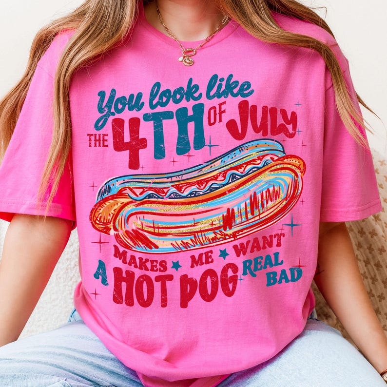 May include: Pink t-shirt with a graphic of a hot dog and the text "You look like the 4th of July makes me want a hot dog real bad." The design features red, blue, and yellow colors.