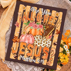 Könnte beinhalten: Ein rechteckiger Leinwanddruck mit vertikalen orangefarbenen und braunen Streifen und dem Text Are You FALL-O-WEEN JESUS? Matthew 4:19. Das Design zeigt Kürbisse, rosa Rosen, ein braunes Buch mit einem Kreuz, Eicheln und herbstliche Blätter.