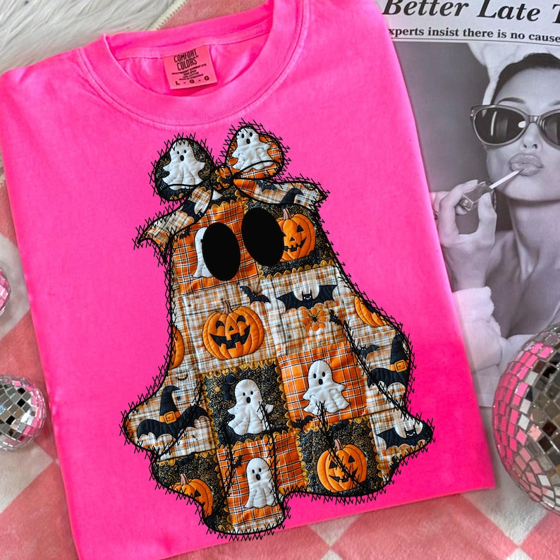 May include: A bright pink Comfort Colors sweatshirt featuring a patchwork ghost design. The ghost is made of orange, black, and white squares with Halloween-themed images. The ghost has large black eyes and is outlined with black stitching.
