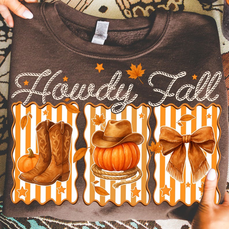 May include: A brown sweatshirt with the words "Howdy Fall" in white script. The design features a cowboy boot, a pumpkin with a cowboy hat, and a bow, all in fall colors. The design is framed with orange and white stripes.