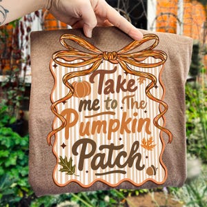 May include: A brown rectangular sign with the text "Take me to The Pumpkin Patch" in orange and brown. The sign has a bow at the top and a pumpkin illustration. The background has vertical stripes.