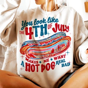 May include: Cream-colored sweatshirt with a colorful graphic of a hot dog and text that reads "You look like the 4th of July. Makes me want a hot dog real bad."