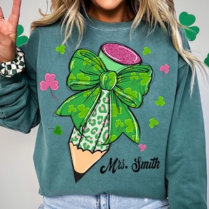 May include: Green sweatshirt with a green and pink pencil with a shamrock bow. The text "Mrs. Smith" is printed on the sweatshirt.