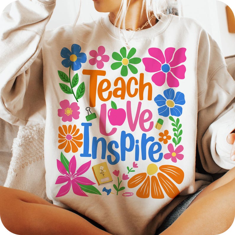 May include: A white sweatshirt with a colorful graphic design featuring flowers, an apple, and the text "Teach Love Inspire".
