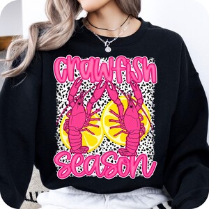 May include: Black sweatshirt with a pink graphic of two crawfish with lemons and the text "Crawfish Season".