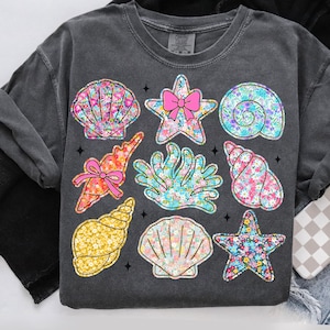 May include: A dark gray t-shirt with a floral print design featuring seashells, starfish, and coral. The design is in shades of pink, blue, and yellow.