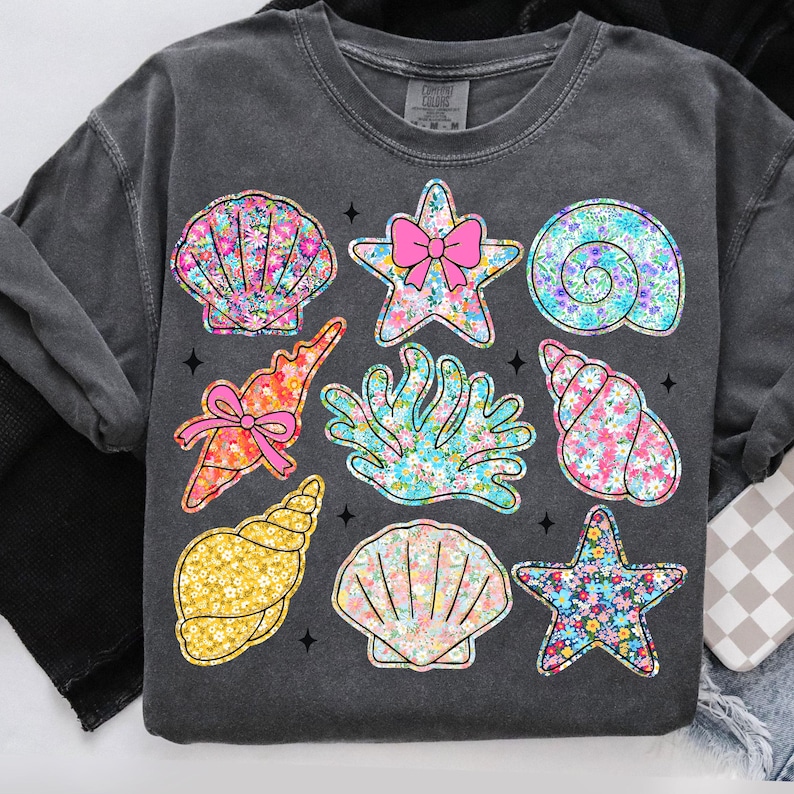 May include: A dark gray t-shirt with a floral print design featuring seashells, starfish, and coral. The design is in shades of pink, blue, and yellow.
