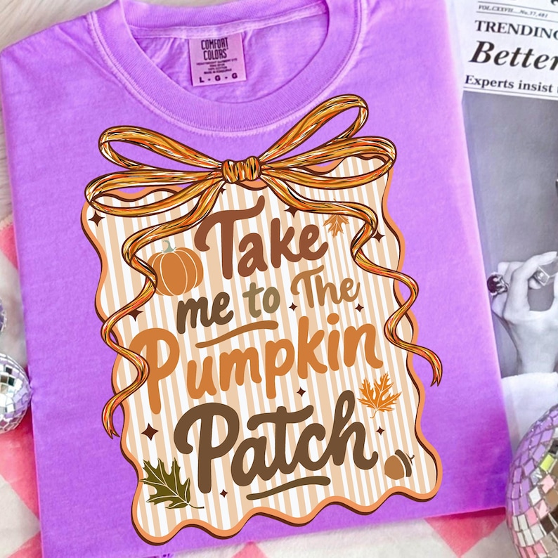 May include: A lilac Comfort Colors t-shirt featuring a decorative design with the text "Take me to The Pumpkin Patch." The design includes a pumpkin, leaves, and a ribbon. The shirt is folded.