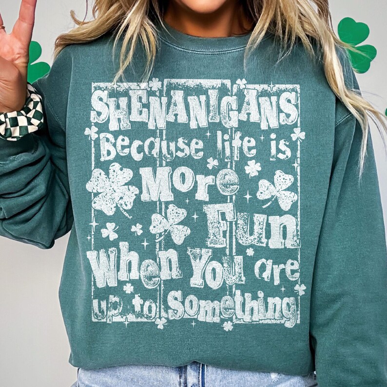 May include: A teal green sweatshirt with the text "SHENANIGANS Because life is MORE Fun When You are up to Something" in white lettering. The design includes shamrocks and stars. The sweatshirt is a casual style.