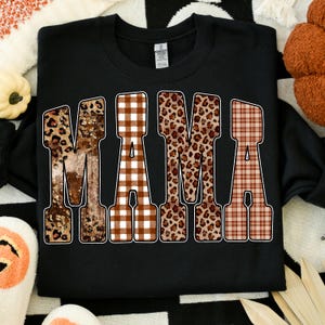 May include: Black sweatshirt with the word "MAMA" in a bold, decorative font. The letters feature a mix of leopard print, brown gingham, and plaid patterns. A cozy and stylish top for mothers.