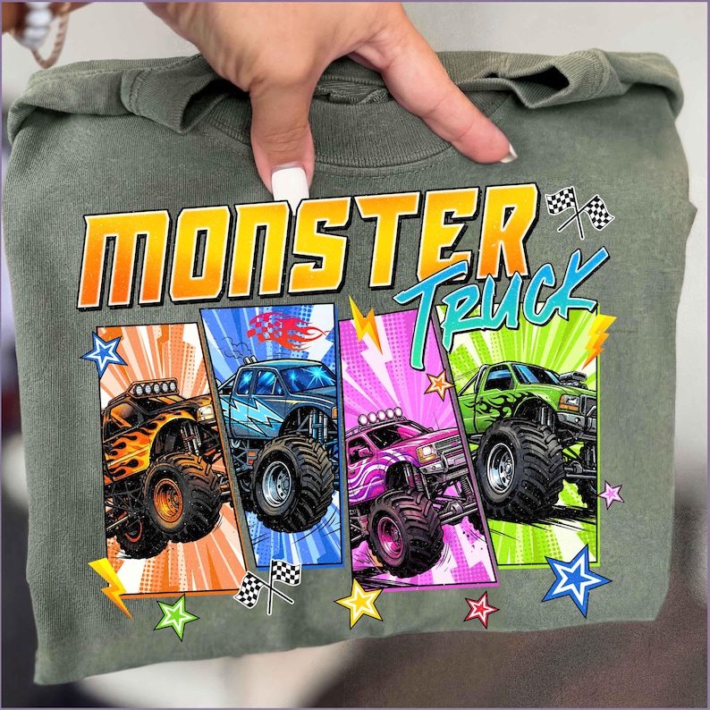 May include: Olive green t-shirt featuring the words "MONSTER TRUCK" in orange and blue. The shirt displays four colorful monster truck illustrations with flames, lightning bolts, and checkered flags. The design is set against a comic book style background.