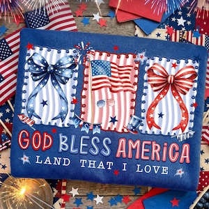 Puede incluir: Una sudadera azul con gr&aacute;ficos patri&oacute;ticos. El dise&ntilde;o incluye un lazo azul, una bandera estadounidense y un lazo rojo, todos enmarcados con un borde festoneado. El texto "GOD BLESS AMERICA" y "LAND THAT I LOVE" se muestra en rojo y azul.