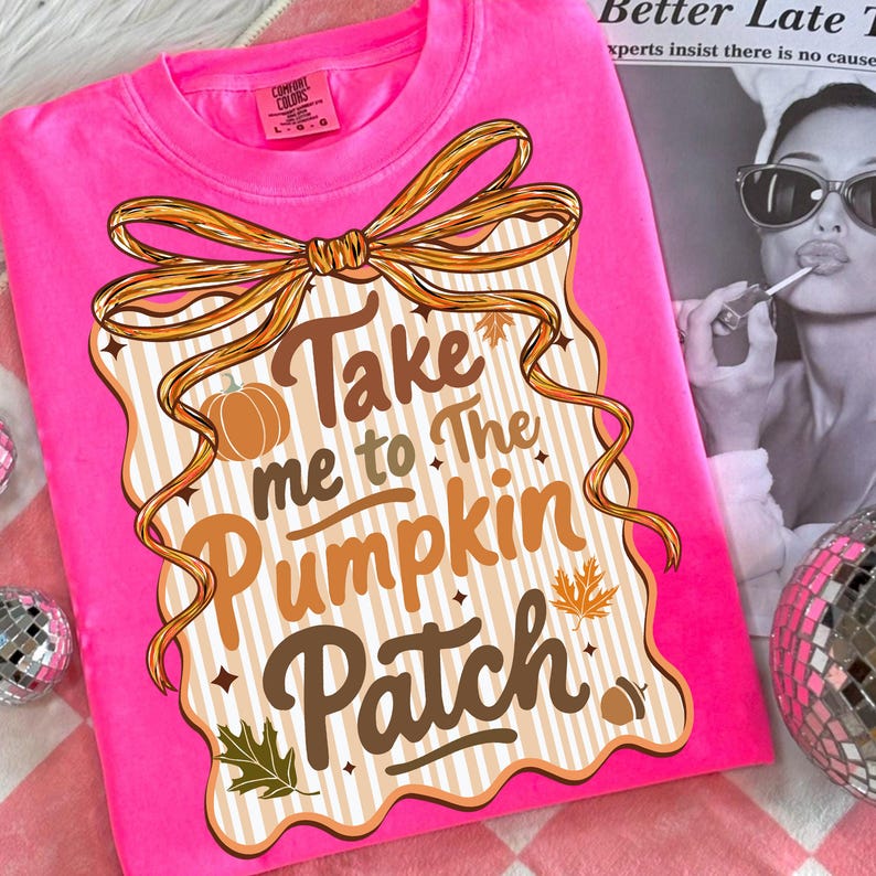 May include: A bright pink t-shirt with the phrase "Take me to The Pumpkin Patch" in brown and orange lettering. The design includes a pumpkin, leaves, and a decorative bow. The shirt is a Comfort Colors brand.