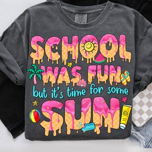 May include: A gray t-shirt with the text "School was fun but it's time for some sun" in pink letters with a waffle cone texture and dripping pink icing. The letters are decorated with summer-themed icons like a watermelon, a seashell, a palm tree, a beach ball, a popsicle, and a sun.