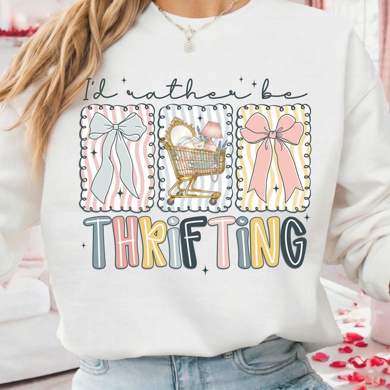 May include: White sweatshirt with the text "I'd rather be thrifting." The design includes three framed illustrations: a bow, a shopping cart, and another bow. The word "THRIFTING" is in colorful block letters.