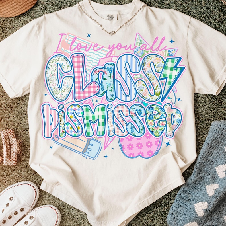 May include: White t-shirt with a colorful graphic that says "I love you all Classy Dismissed". The graphic is made up of different patterns, including plaid, floral, and stripes.
