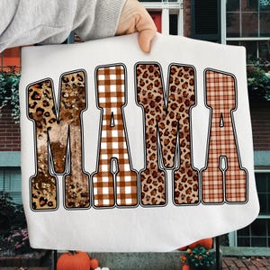 May include: White sweatshirt featuring the word "MAMA" in large, bold letters. Each letter has a unique pattern: leopard print, brown gingham, leopard print, and a plaid design. The letters are outlined in black.