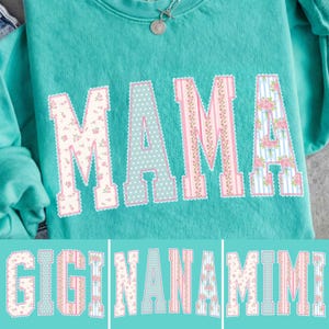 Könnte beinhalten: Ein türkisfarbenes Sweatshirt mit dem Wort "MAMA" in großen, dekorativen Buchstaben. Die Buchstaben sind mit floralen, gepunkteten und gestreiften Designs in Rosa und Weiß gemustert. Darunter stehen die Wörter "GIGI", "NANA" und "MIMI" im gleichen Stil.