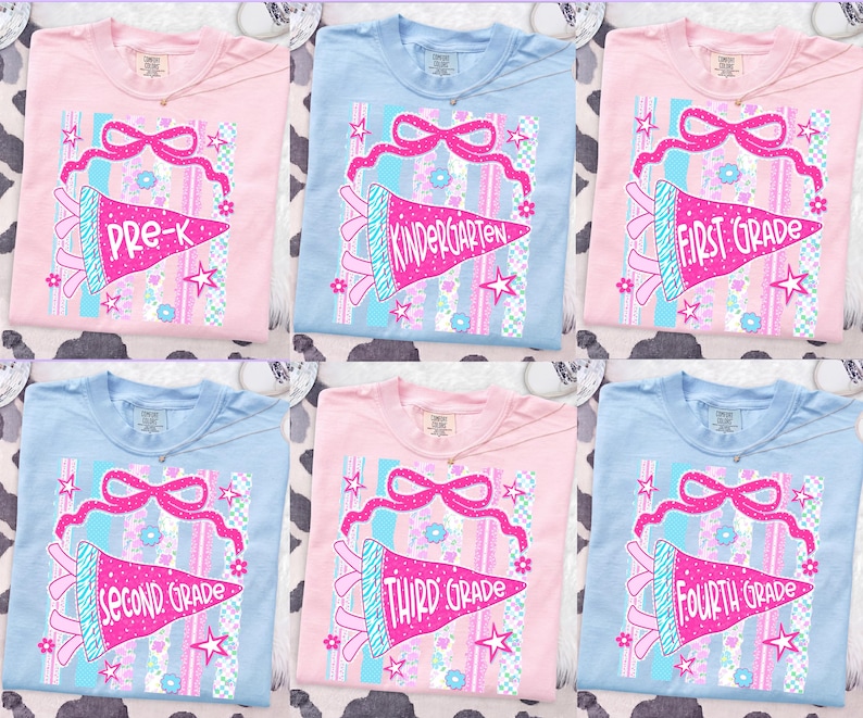 May include: Six pastel-colored t-shirts with school grade graphics. Each shirt features a pennant design with text indicating the grade level, Pre-K through Fourth Grade. The pennants are pink with blue accents and star details.