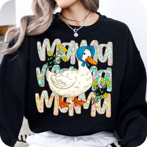 May include: Black sweatshirt featuring the word "MAMA" repeated three times in a floral design. A white duck wearing a blue bonnet is in the centre. The duck has an orange beak and feet. Yellow flowers and green leaves are also in the design.