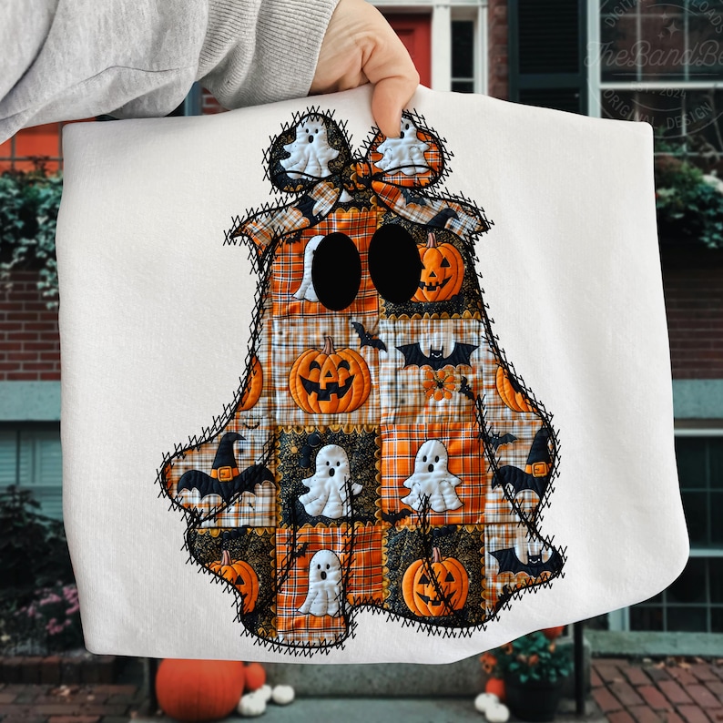 May include: A white Halloween-themed decorative pillow in the shape of a ghost. The ghost design features a patchwork pattern with pumpkins, bats, and ghost figures in orange, black, and white. The edges are outlined with black stitching.