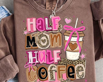 May include: A brown sweatshirt featuring the text "Half Mom Half Coffee" in pink, brown, and black. The design includes a coffee cup with a pink bow and a heart, along with star and leopard print accents. A silver necklace is visible.