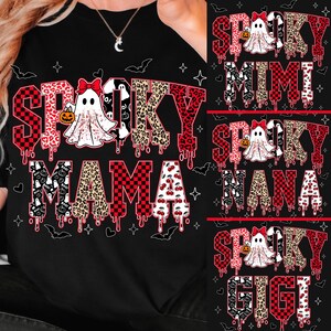 May include: Black t-shirt with a Halloween-themed design. The shirt features the word "Spooky" in a red and black checkered pattern, with a ghost and pumpkin graphic. Below, the word "Mama" is displayed in a leopard print and cherry pattern.