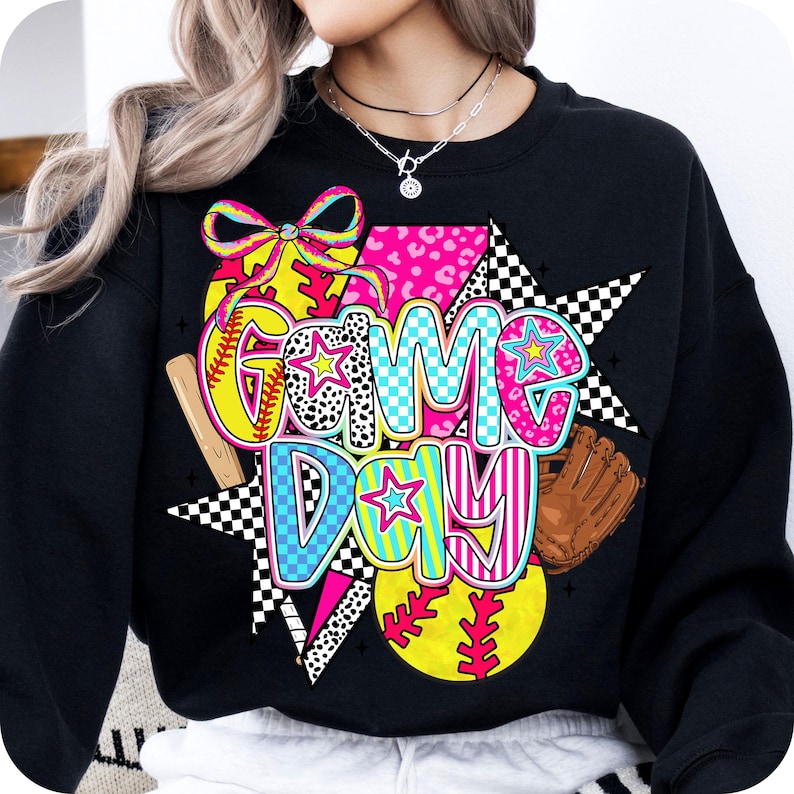 May include: Black sweatshirt with a colorful graphic design featuring the words "Game Day" with baseballs, bats, and stars.
