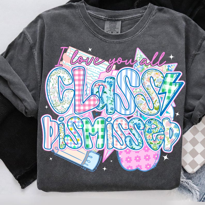 May include: A dark gray t-shirt with a patchwork design featuring the text "I love you all Classy Dismissed". The design includes a pencil, a lightning bolt, and a pink apple.