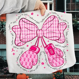 May include: White fabric with a pink bow and boxing gloves design. The bow and gloves are decorated with pink ribbons. The words "Together we fight" are written around the design.