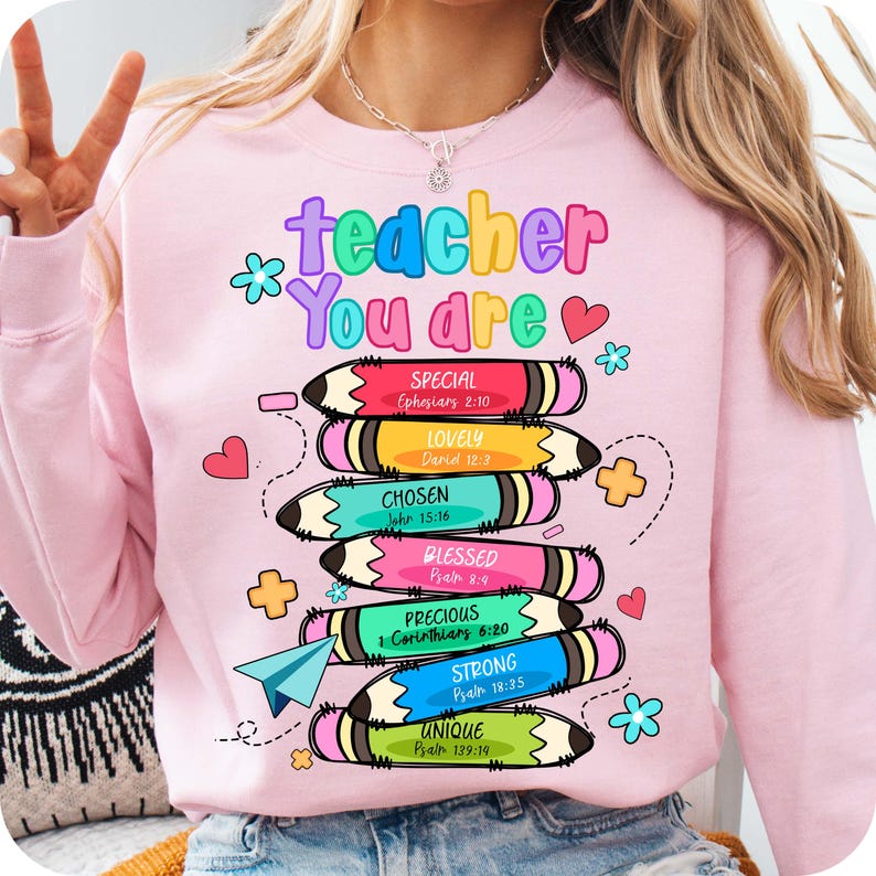 May include: A light pink sweatshirt with the words "teacher You are" in colorful bubble letters. Below are stacked pencils with words like "Special", "Lovely", and "Chosen". The design includes hearts, flowers, and a paper airplane.
