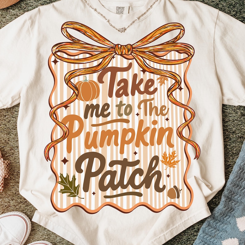 May include: Cream-colored t-shirt with a fall-themed graphic. The design features the text "Take me to The Pumpkin Patch" in brown and orange, with a pumpkin, leaves, and a bow. The shirt is made of a soft material.