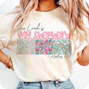 May include: A white t-shirt with a floral design and the text "The Lord is My Shepherd" in pink lettering. The text "Psalms 23:1" is also included in smaller lettering.