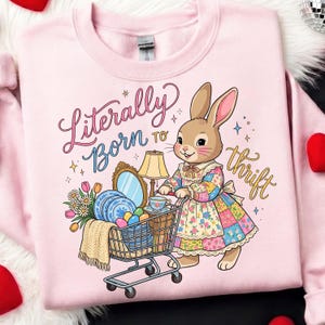 May include: Pink sweatshirt with a graphic of a cartoon bunny pushing a shopping cart filled with vintage items. The text "Literally Born to thrift" is written in script. The bunny wears a patchwork dress.
