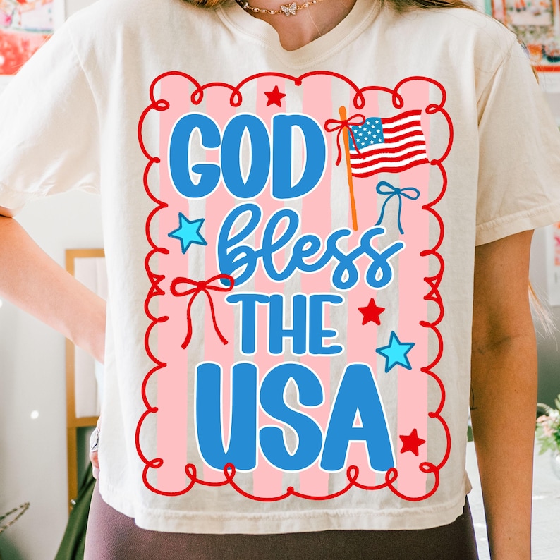 Puede incluir: Camiseta color crema con un dise&ntilde;o patri&oacute;tico. El gr&aacute;fico incluye el texto "GOD bless THE USA" en azul, con un fondo de rayas rojas y blancas, estrellas y una peque&ntilde;a bandera estadounidense.