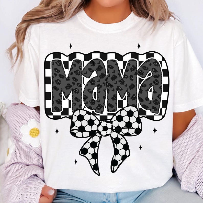 May include: White t-shirt with a black and white chequered design featuring the word "Mama" in a black and white leopard print. A black and white football bow is below the word.