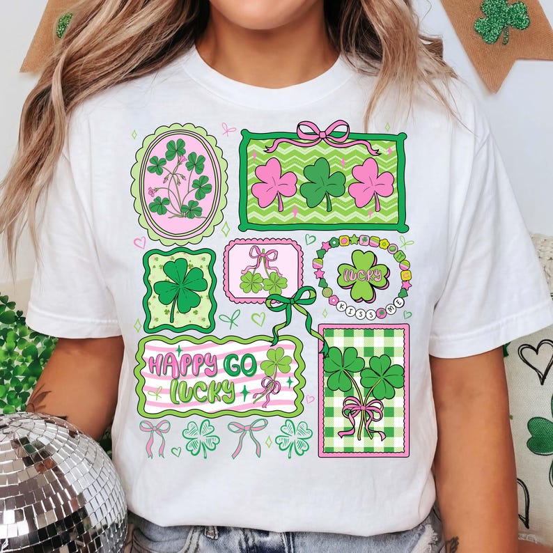 Op de afbeelding: Wit T-shirt met een St. Patrick's Day ontwerp. Het ontwerp bevat omlijste klavers in groen en roze, en de woorden "Happy Go Lucky". Een casual kledingstuk, perfect om St. Patrick's Day te vieren.